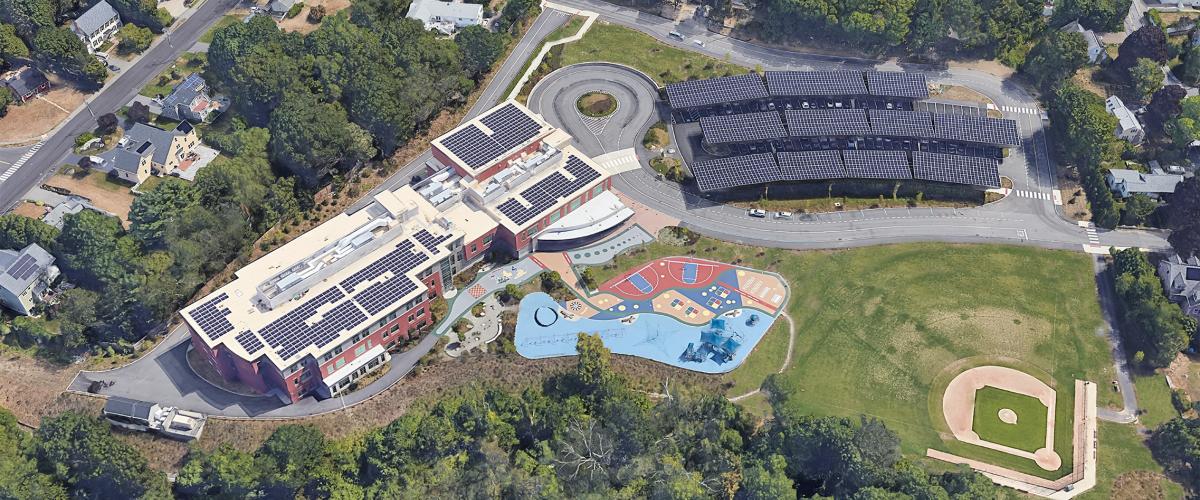 Aerial view of Maria Hastings Elementary School showing rooftop solar arrays and solar canopies above parking area