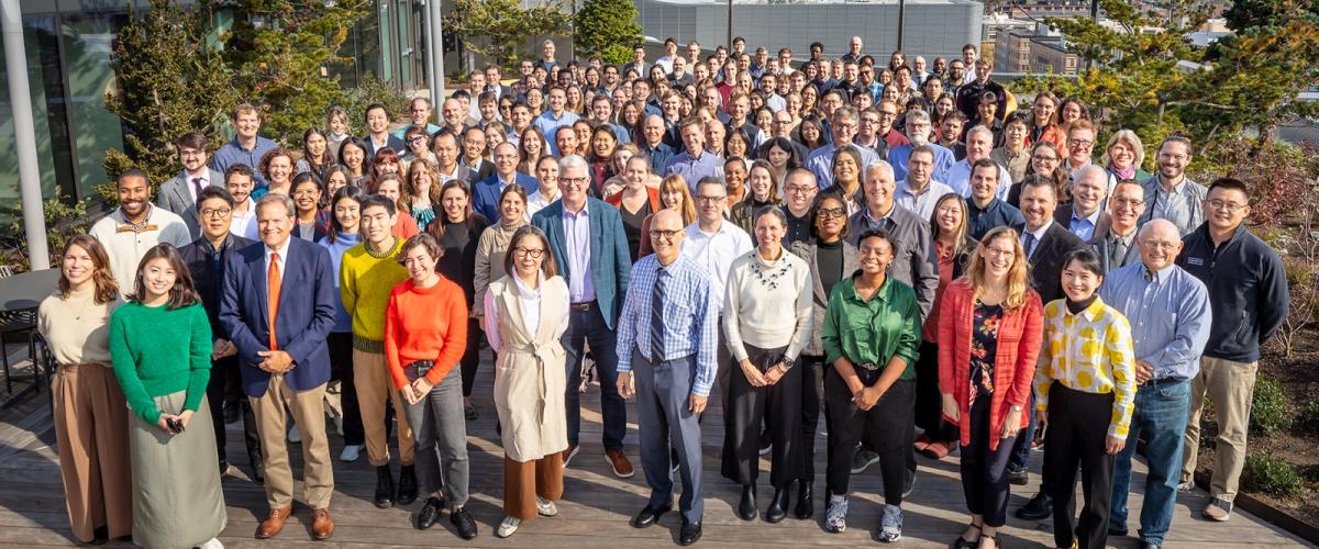 Large group photo of 100+ staff on a roof top overlooking the Boston skyline