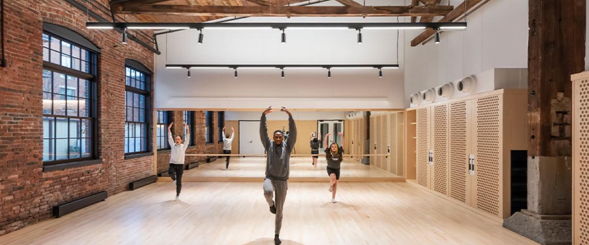 Dance rehearsal space showing historical brick on one exterior wall and wood beams above and three people dancing.