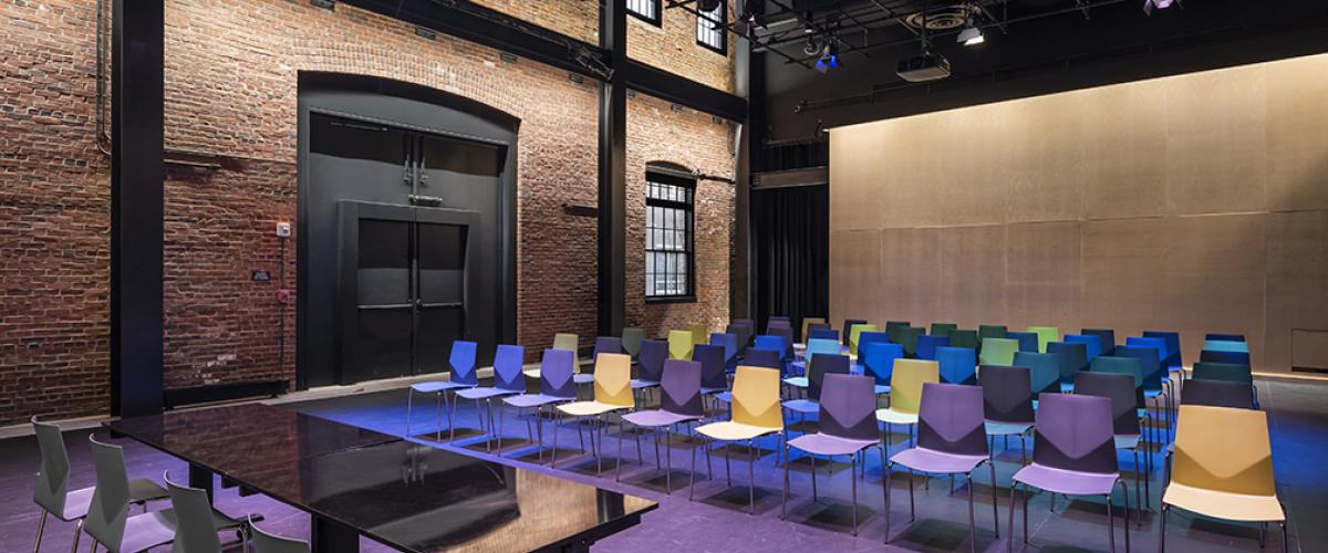 Black box performance space with brick exterior wall and colorful chairs set up for a lecture.