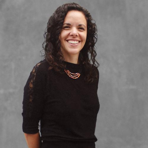 Woman with dark curly hair dressed in black, smiling.