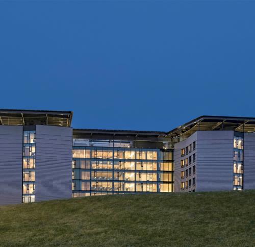 Exterior evening photo of building appearing over a grassy hill